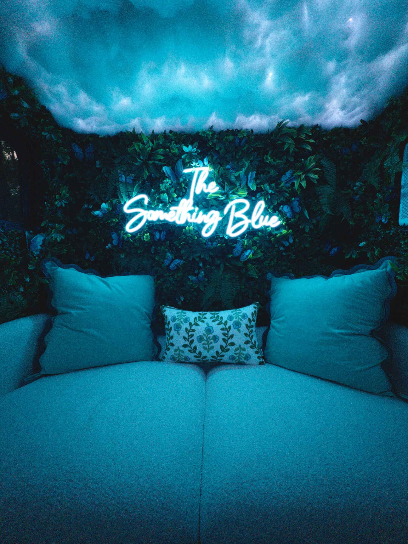 Neon The Something Blue sign above the booth sofa and grass wall