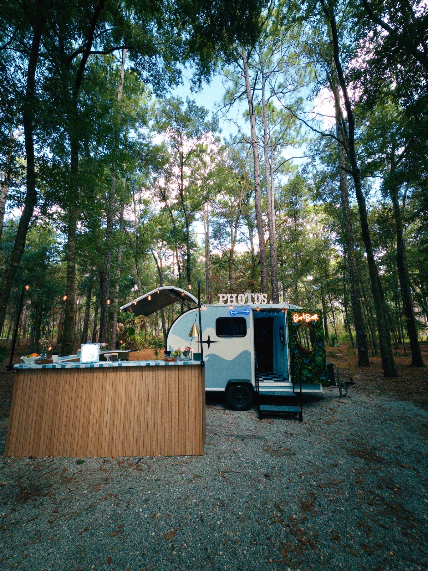 The Something Blue camper and L-shaped bar set up in the pines